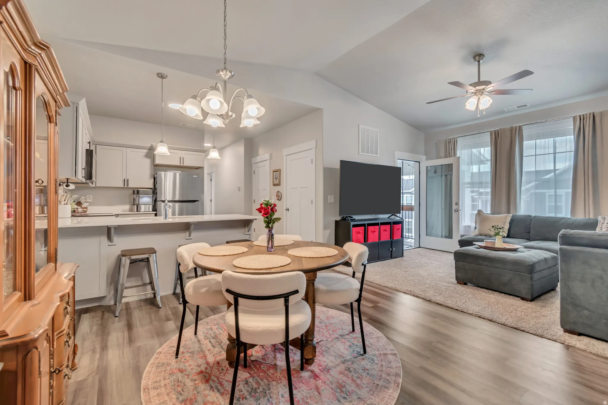 Open-concept living space featuring wood-finish flooring, a kitchen with light cabinetry and stainless steel appliances, a breakfast bar, and a dining area with an overhead chandelier