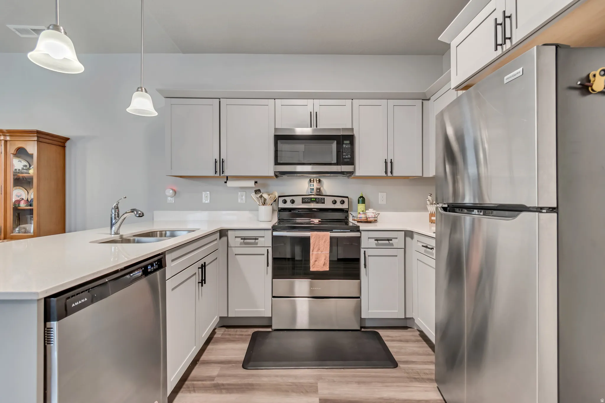 Modern kitchen featuring light gray cabinetry with black hardware, stainless steel appliances, a double basin sink, and wood-finish flooring