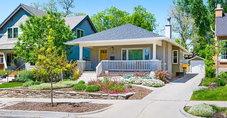 Craftsman-style home featuring a covered front porch with white railings, a concrete driveway, a detached garage, and a landscaped front yard with a stone retaining wall