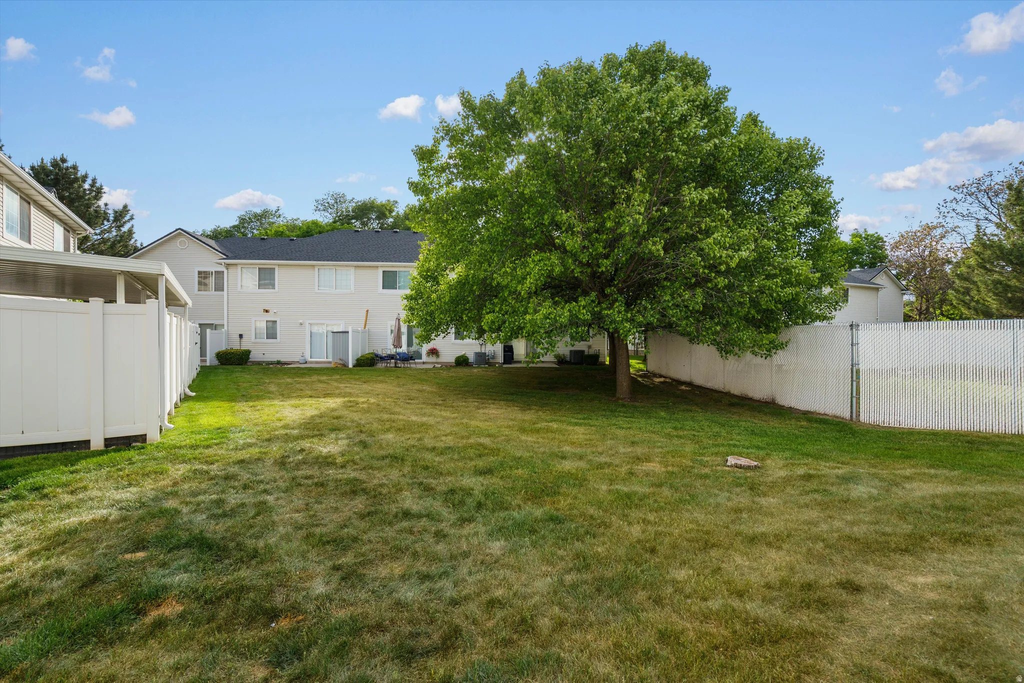Expansive backyard featuring a mature tree, extensive lawn space, and white privacy fencing