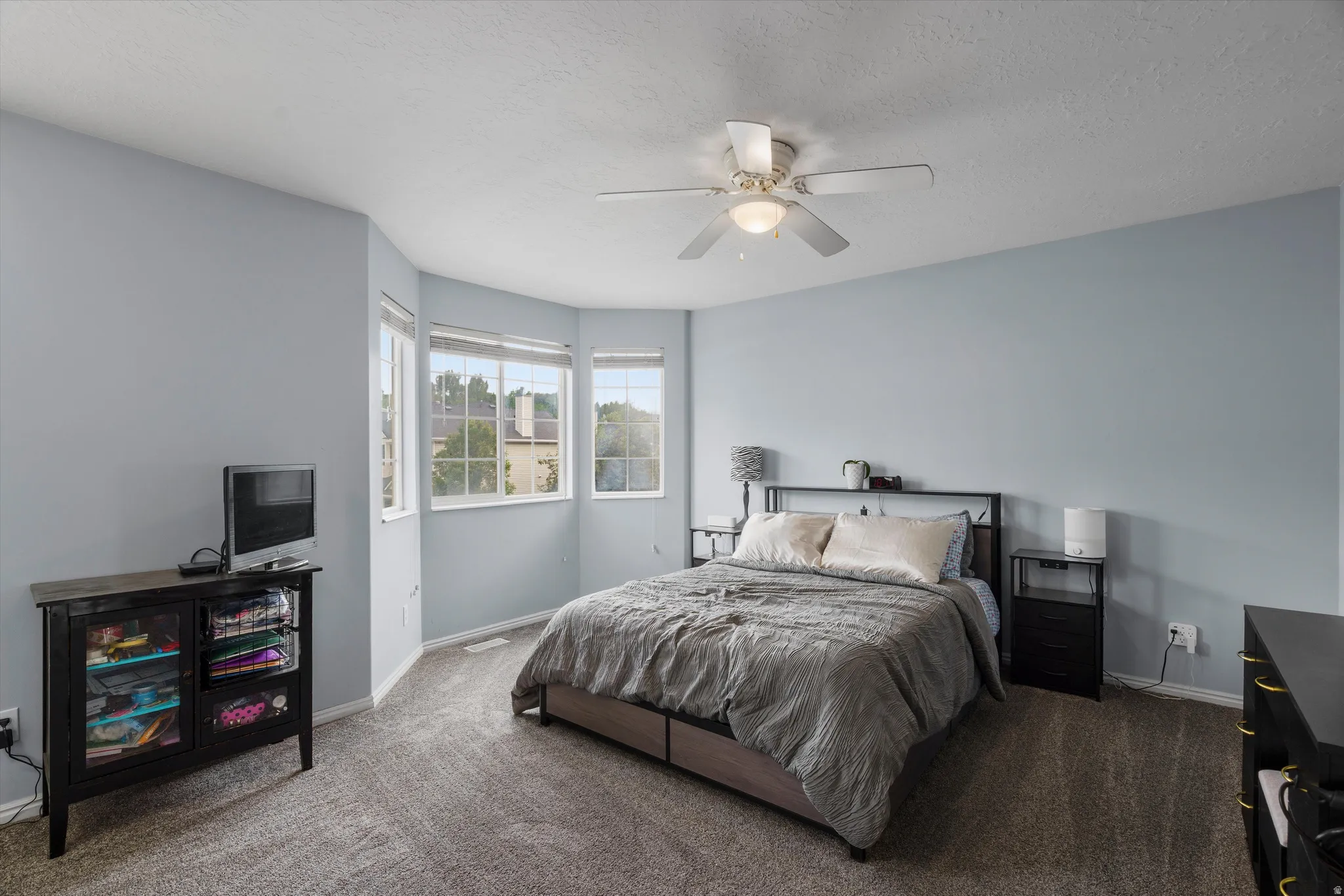 Oversized primary bedroom featuring a bay window with multiple panes, fan with integrated lighting, and white trim