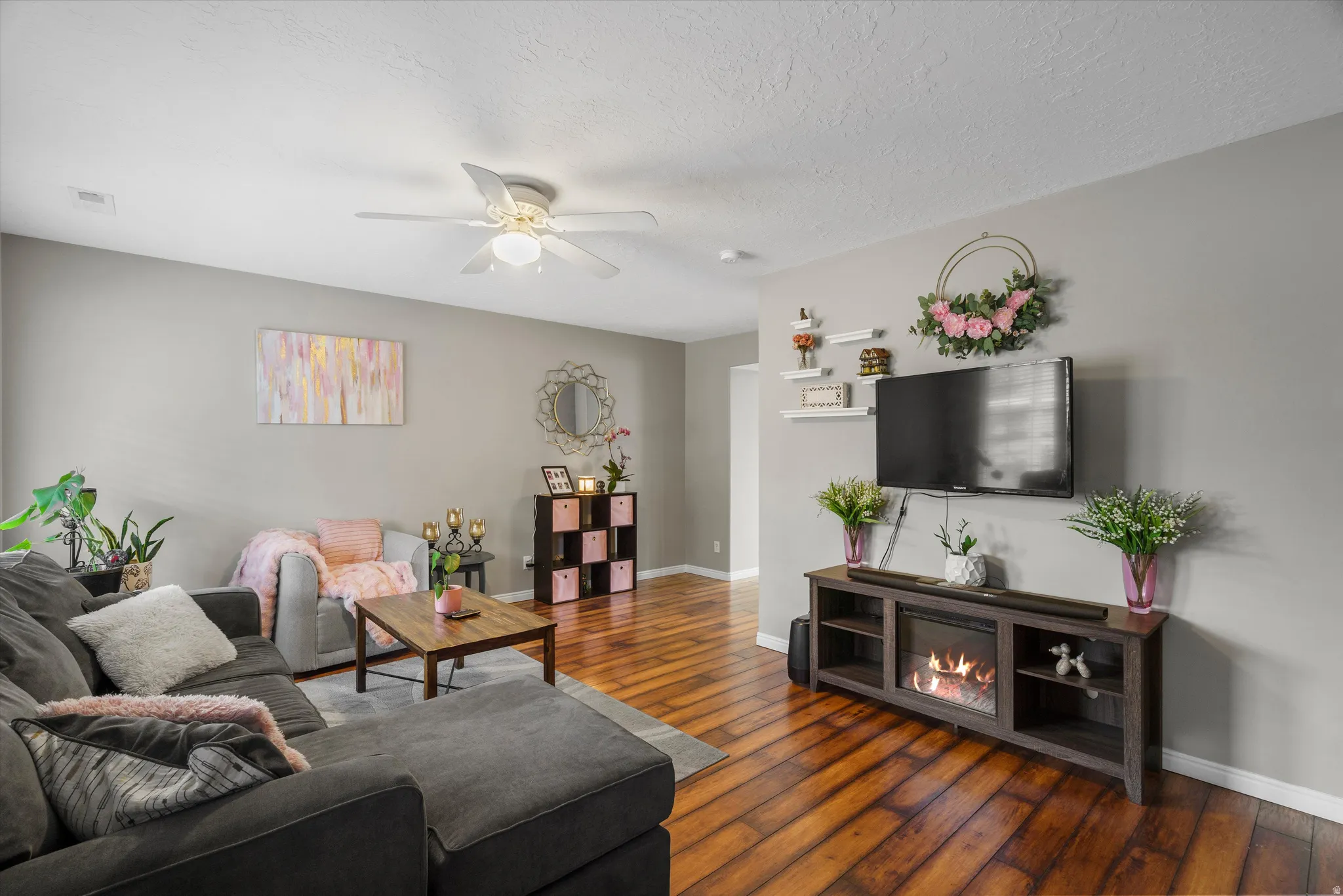 Living area with laminate flooring, light gray wall paint, and a ceiling fan with integrated lighting