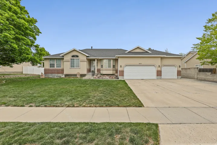Ranch-style residence featuring a stucco and brick facade, a two-car garage, an additional single-car garage, a concrete driveway, and a front lawn with mature trees