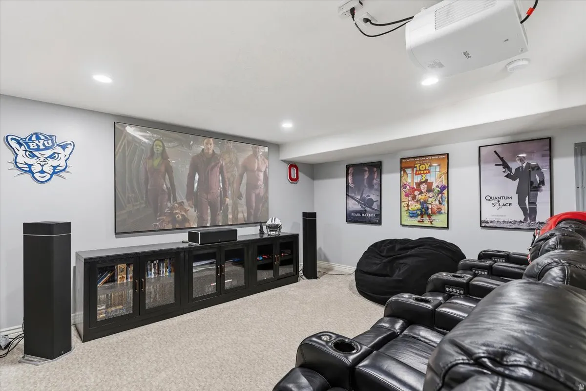 Dedicated media room featuring a large projection screen, mounted projector, recessed lighting, and light-colored carpeting