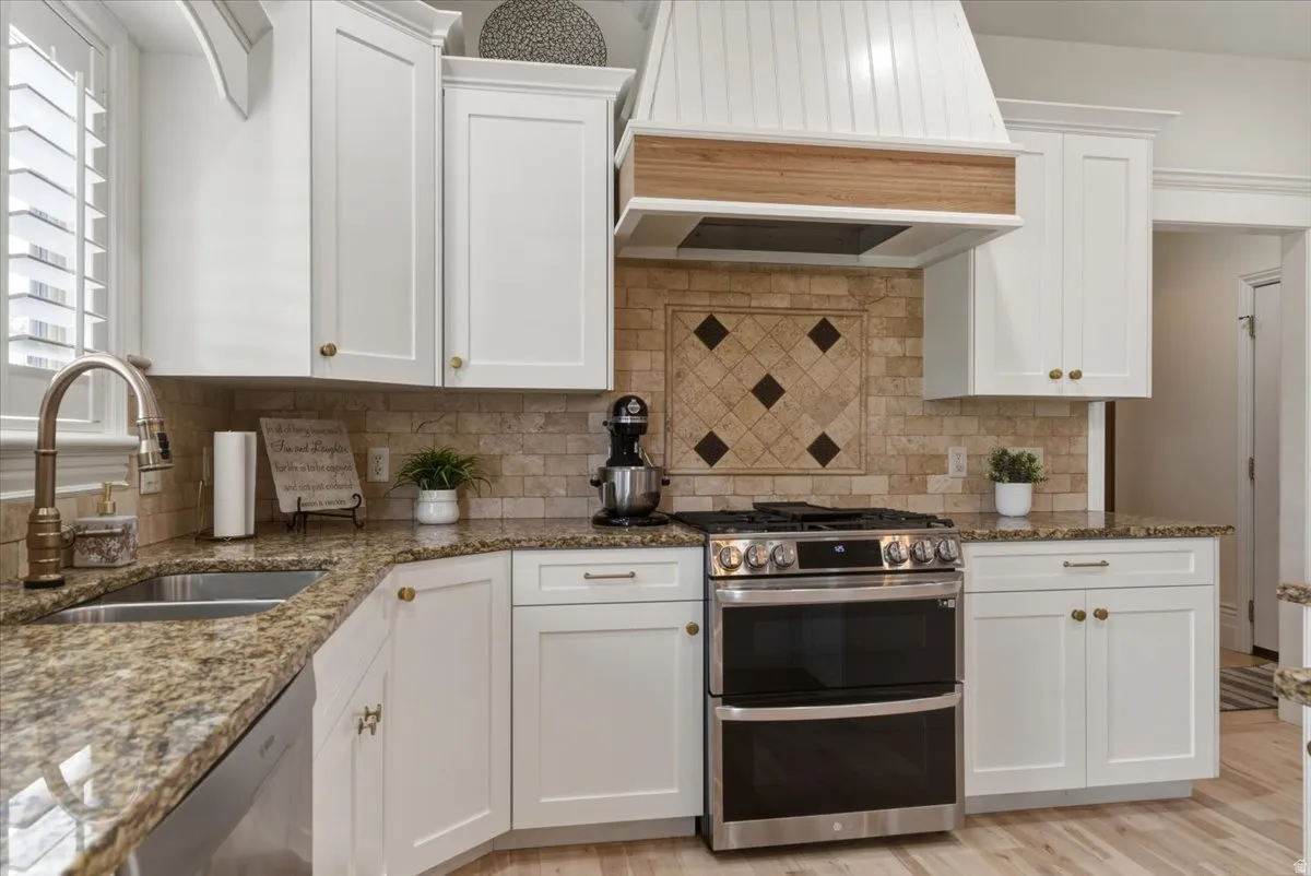 Kitchen featuring white shaker cabinetry, granite countertops, tile backsplash with decorative inset, and stainless steel double oven range