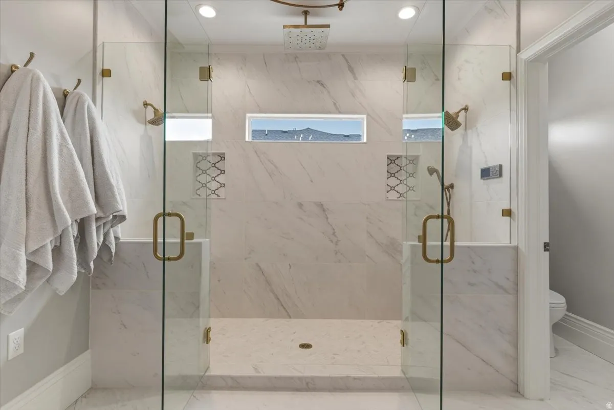 Dual-entry glass shower enclosure featuring marble-finish tile, recessed lighting, and brass-tone fixtures