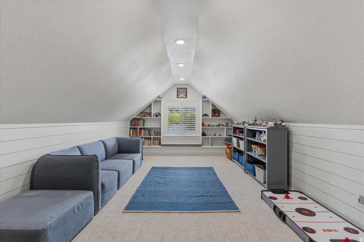 Finished attic space featuring recessed lighting, a window with plantation shutters, built-in shelving, carpet flooring, and shiplap wall detailing