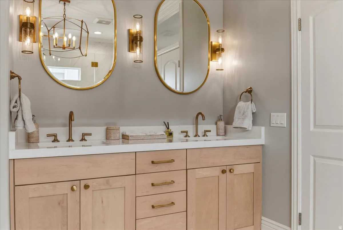 Dual vanity with light wood cabinetry, white countertop, and gold-toned hardware