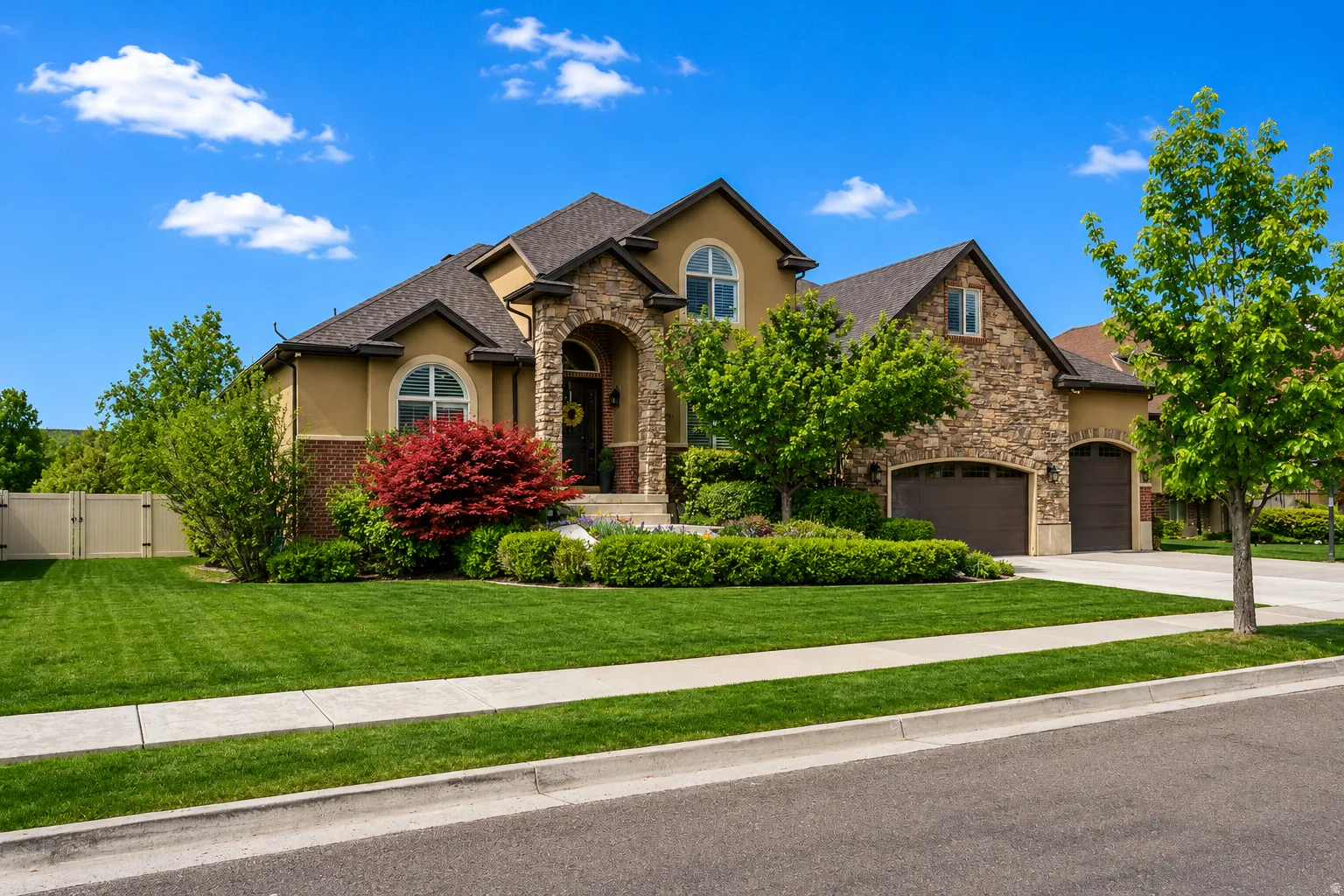 Stucco and stone facade home featuring an arched entry, two-car garage, established landscaping, and a fenced side yard