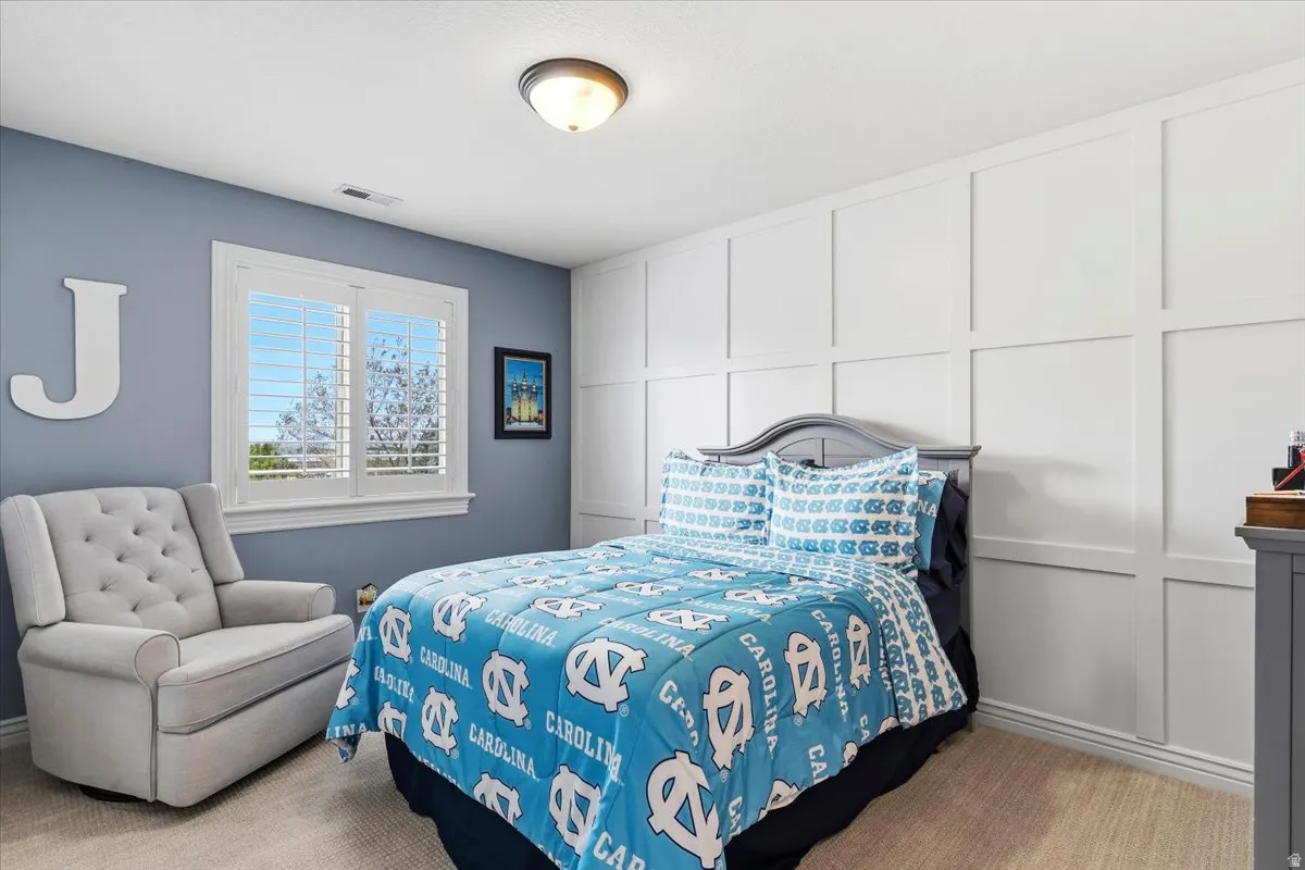 Room featuring a window with white louvered shutters, a paneled accent wall, a flush-mount ceiling light fixture, and neutral-toned carpeting