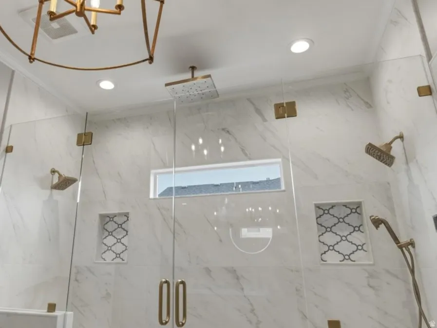 Spacious shower enclosure featuring full-height marble-look tile, frameless glass panels with brass-finish hardware, and a built-in bench