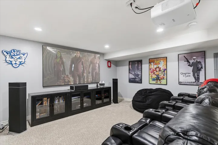 Dedicated media room featuring a large projection screen, mounted projector, recessed lighting, and light-colored carpeting