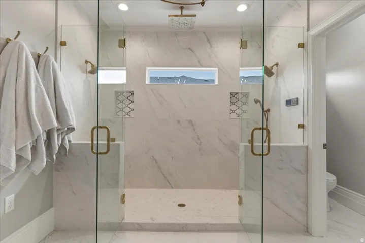 Dual-entry glass shower enclosure featuring marble-finish tile, recessed lighting, and brass-tone fixtures
