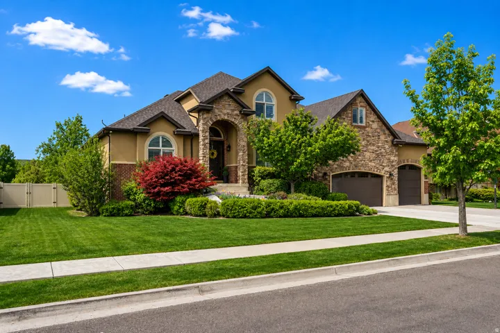 Stucco and stone facade home featuring an arched entry, two-car garage, established landscaping, and a fenced side yard