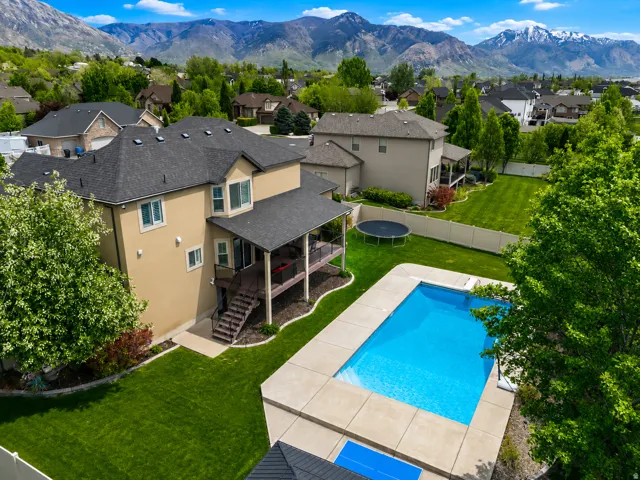 Expansive backyard featuring a rectangular swimming pool with concrete surround, manicured lawn, and mature trees