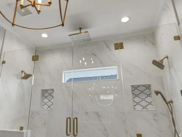 Spacious shower enclosure featuring full-height marble-look tile, frameless glass panels with brass-finish hardware, and a built-in bench