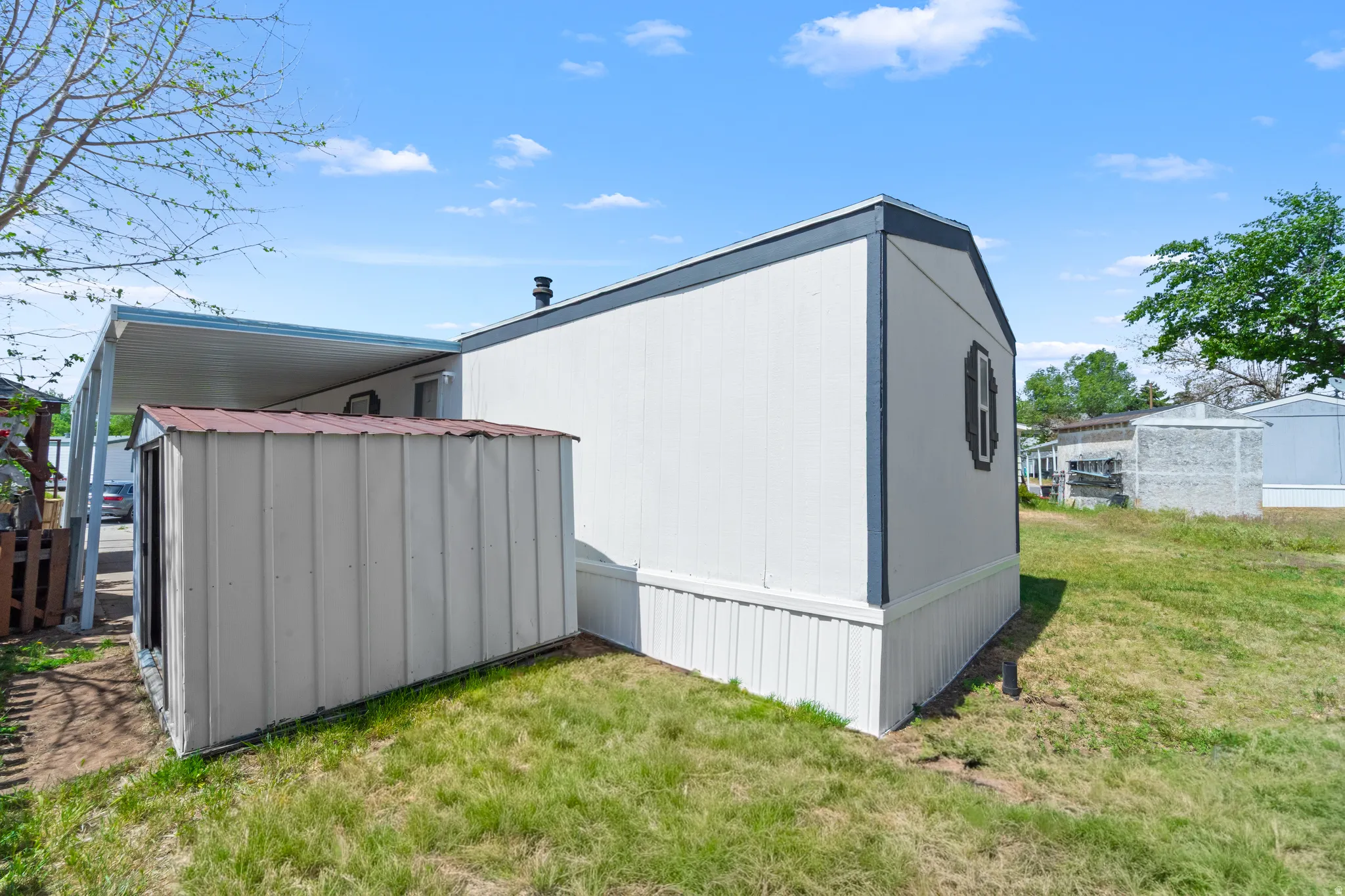 White vertical siding exterior with dark trim accents, featuring a side storage shed and an attached carport