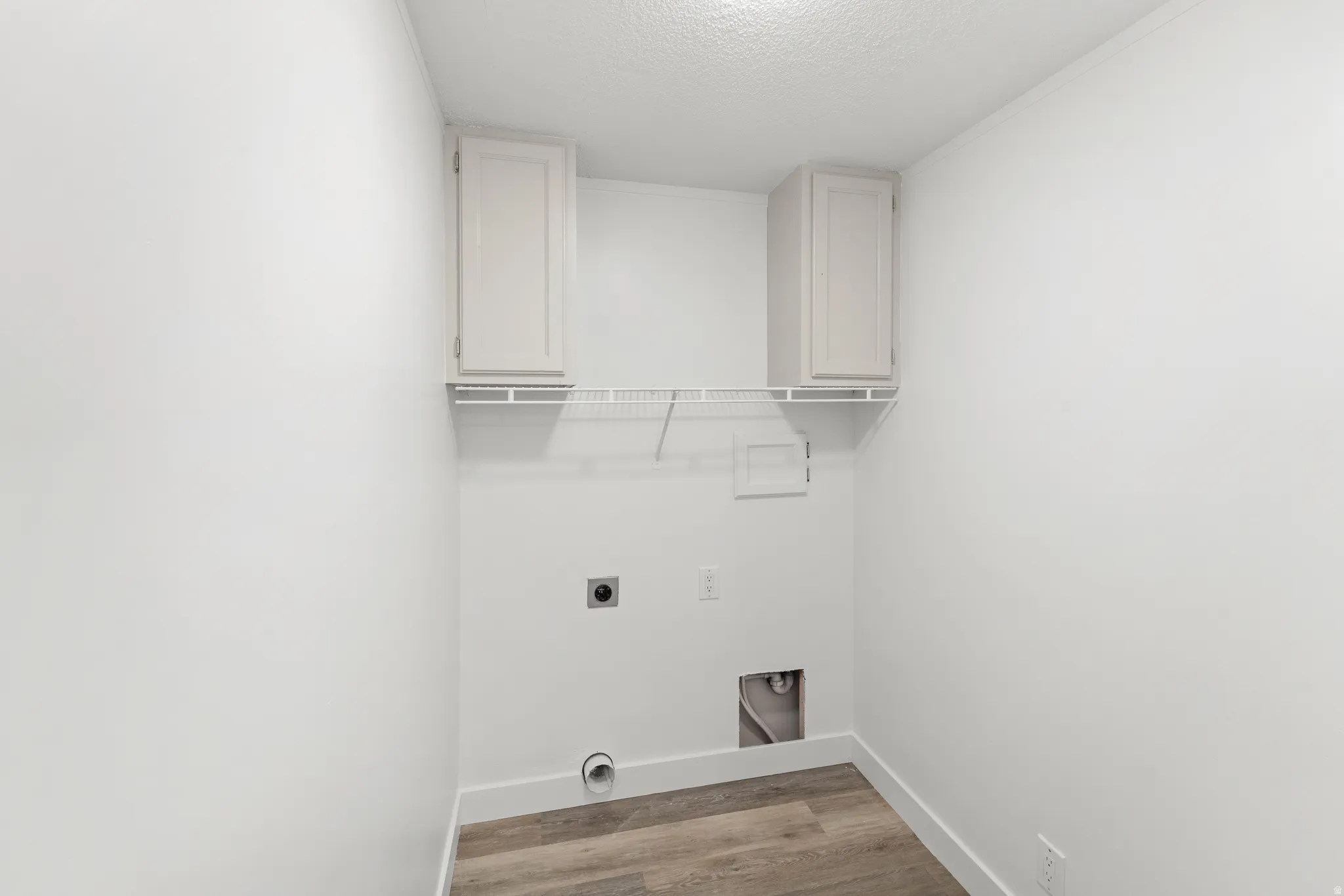 Dedicated utility space featuring neutral wall paint, wood-finish flooring, two upper cabinets, and a wire shelf
