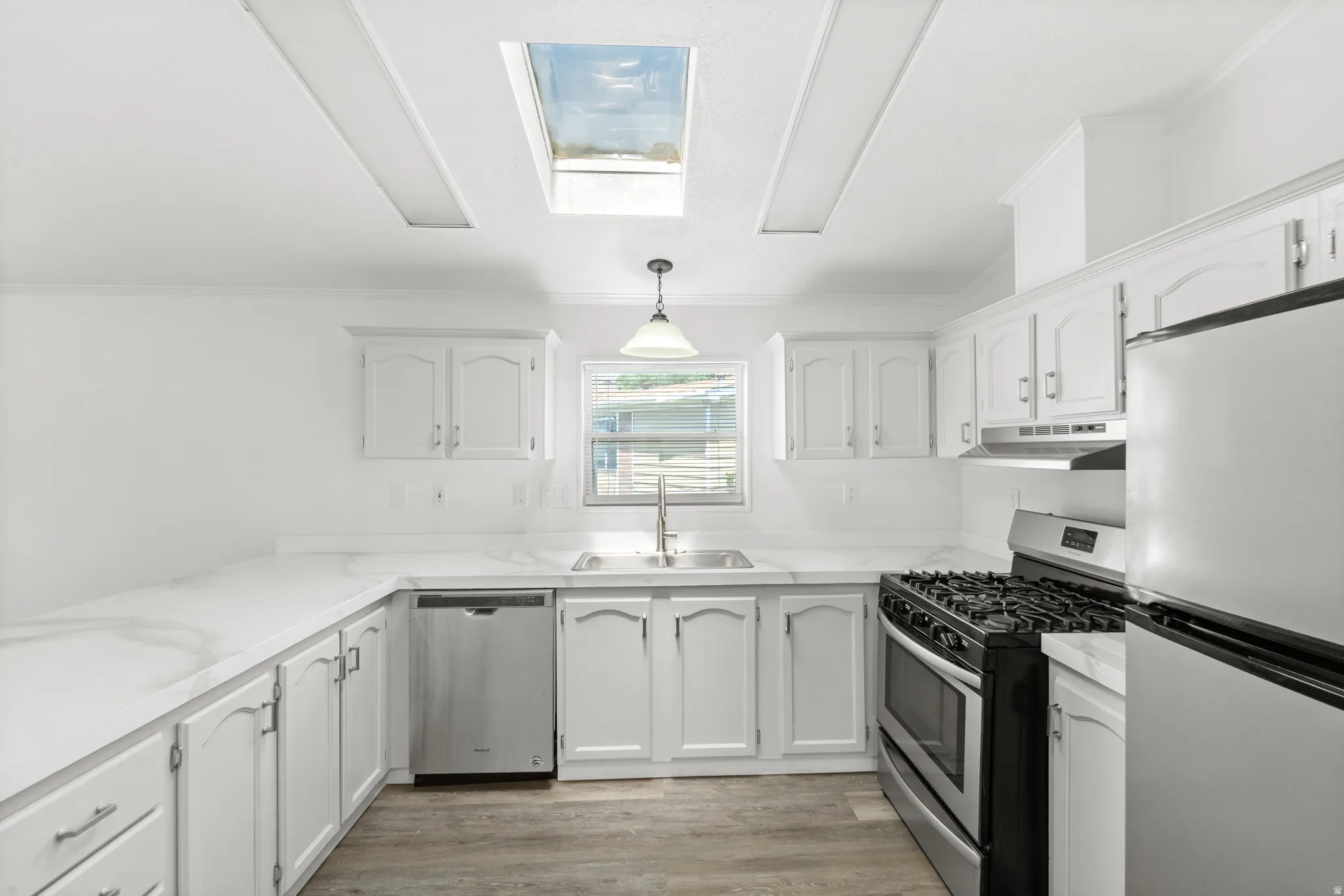 Kitchen featuring white cabinetry, white countertops, stainless steel appliances, wood-finish flooring, and a skylight