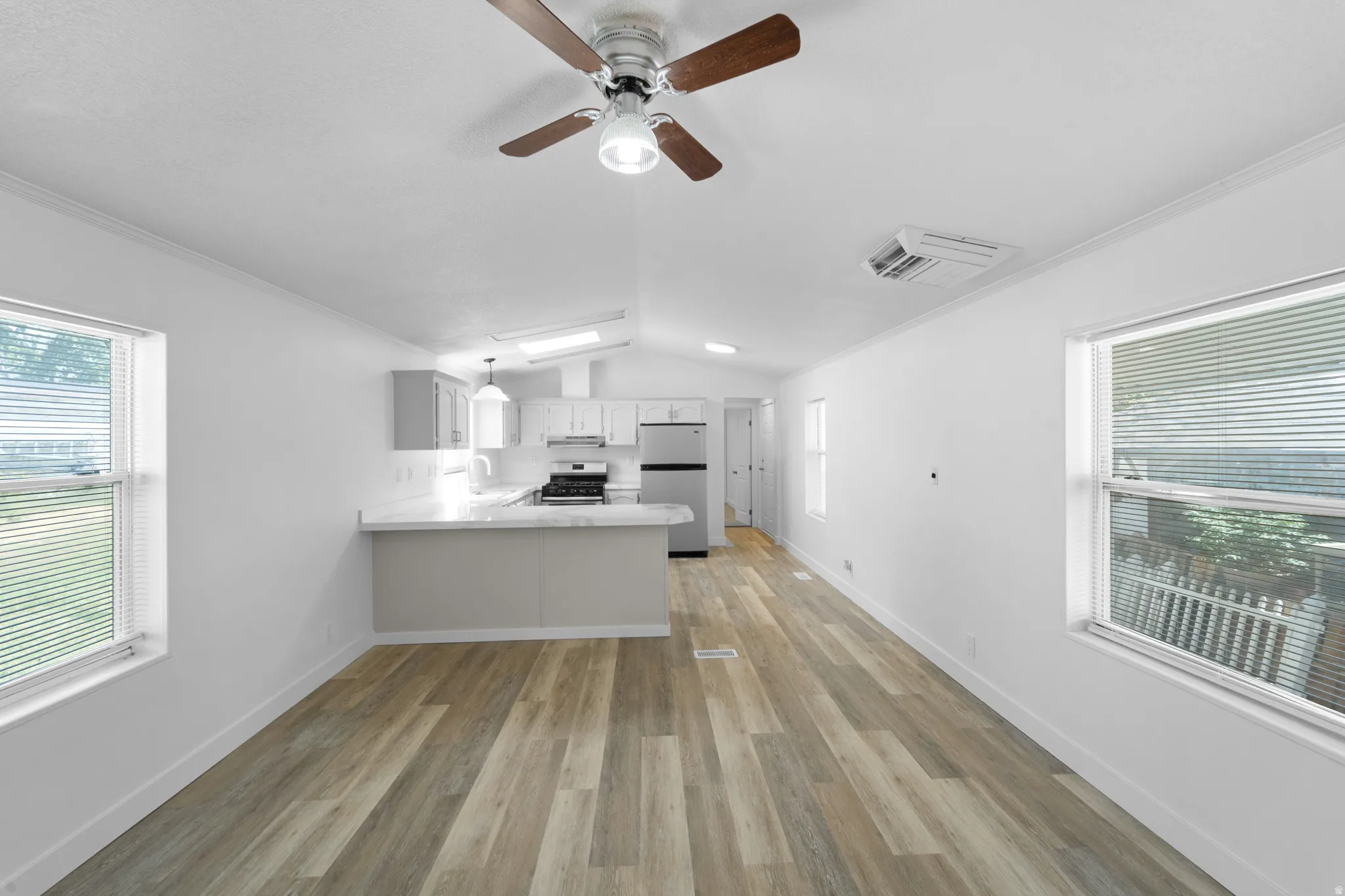 Open-concept living space with wood-finish flooring, a contemporary ceiling fan, and abundant natural light from multiple windows