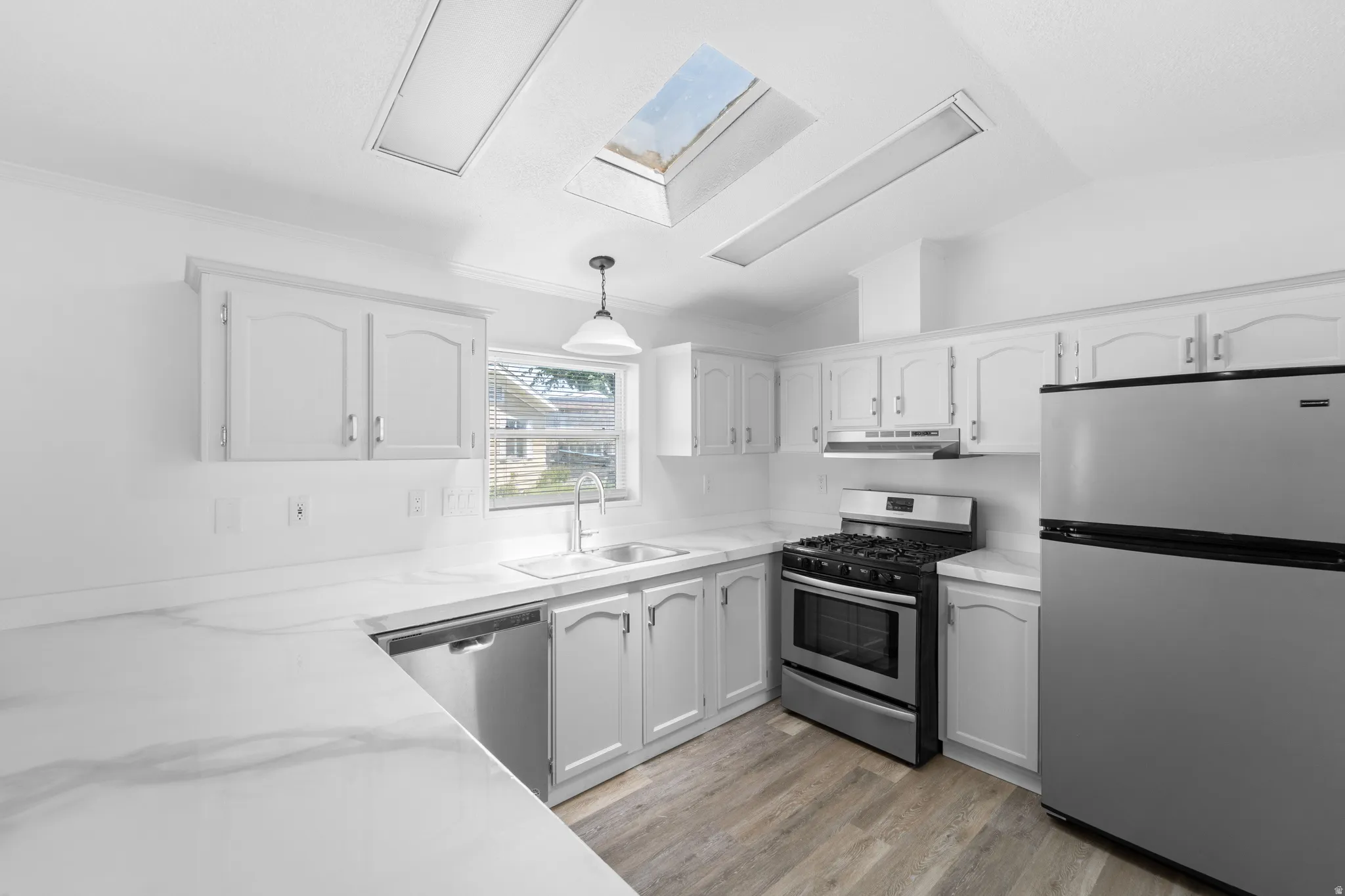 Kitchen featuring skylights, wood-finish flooring, white cabinetry, a double basin sink, and stainless steel appliances