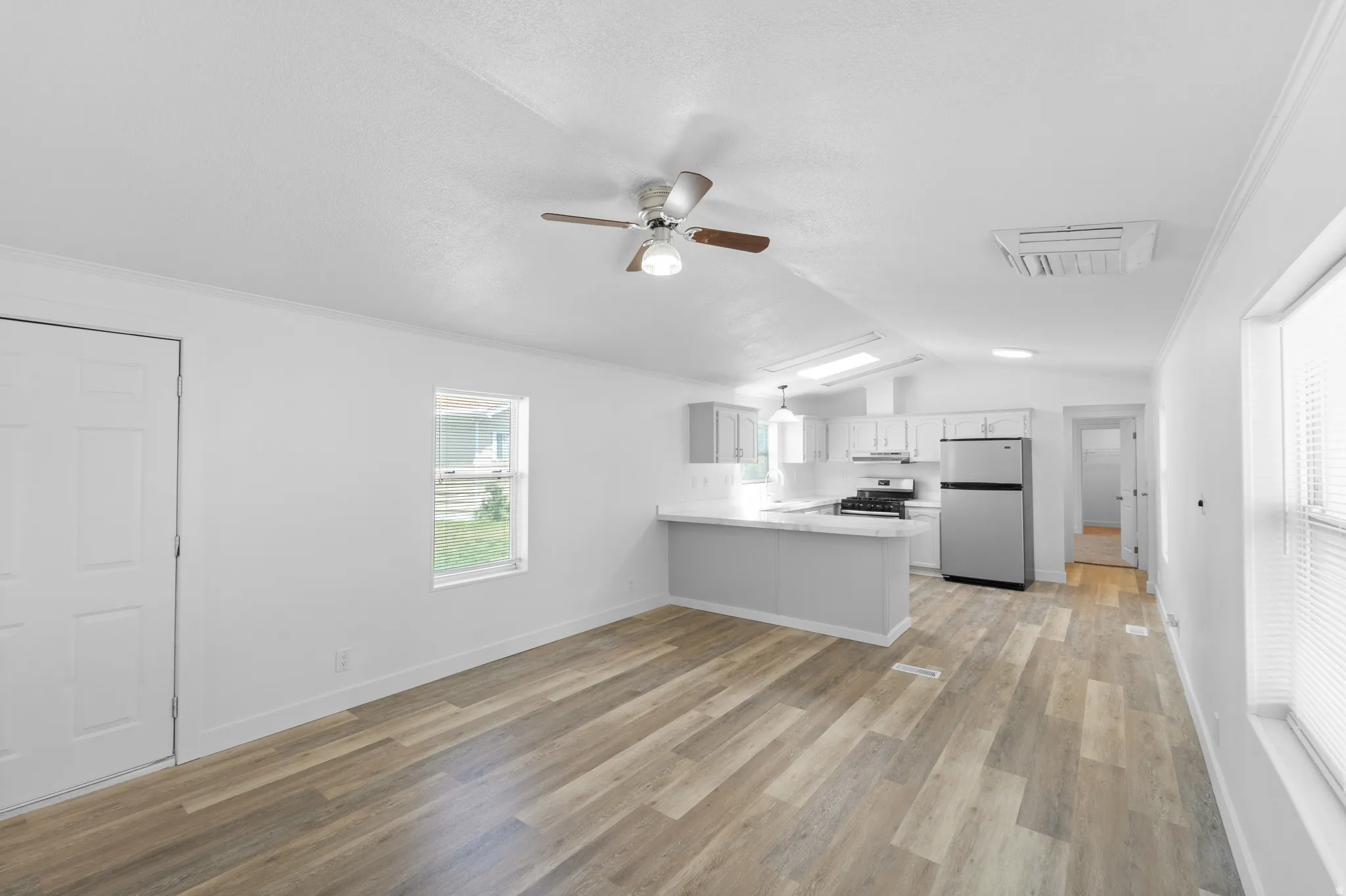 Open-concept living space featuring wood-finish flooring, a ceiling fan, and a kitchen with stainless steel appliances, light cabinetry, and a breakfast bar