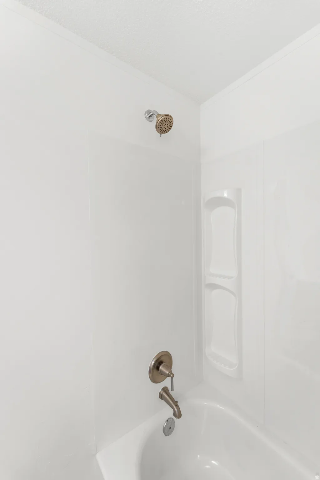 White tub and shower combination with brushed nickel fixtures and built-in shelving