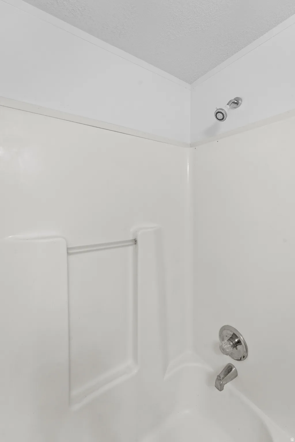 White bathtub and shower surround with integrated soap dish, chrome shower head, and chrome faucet
