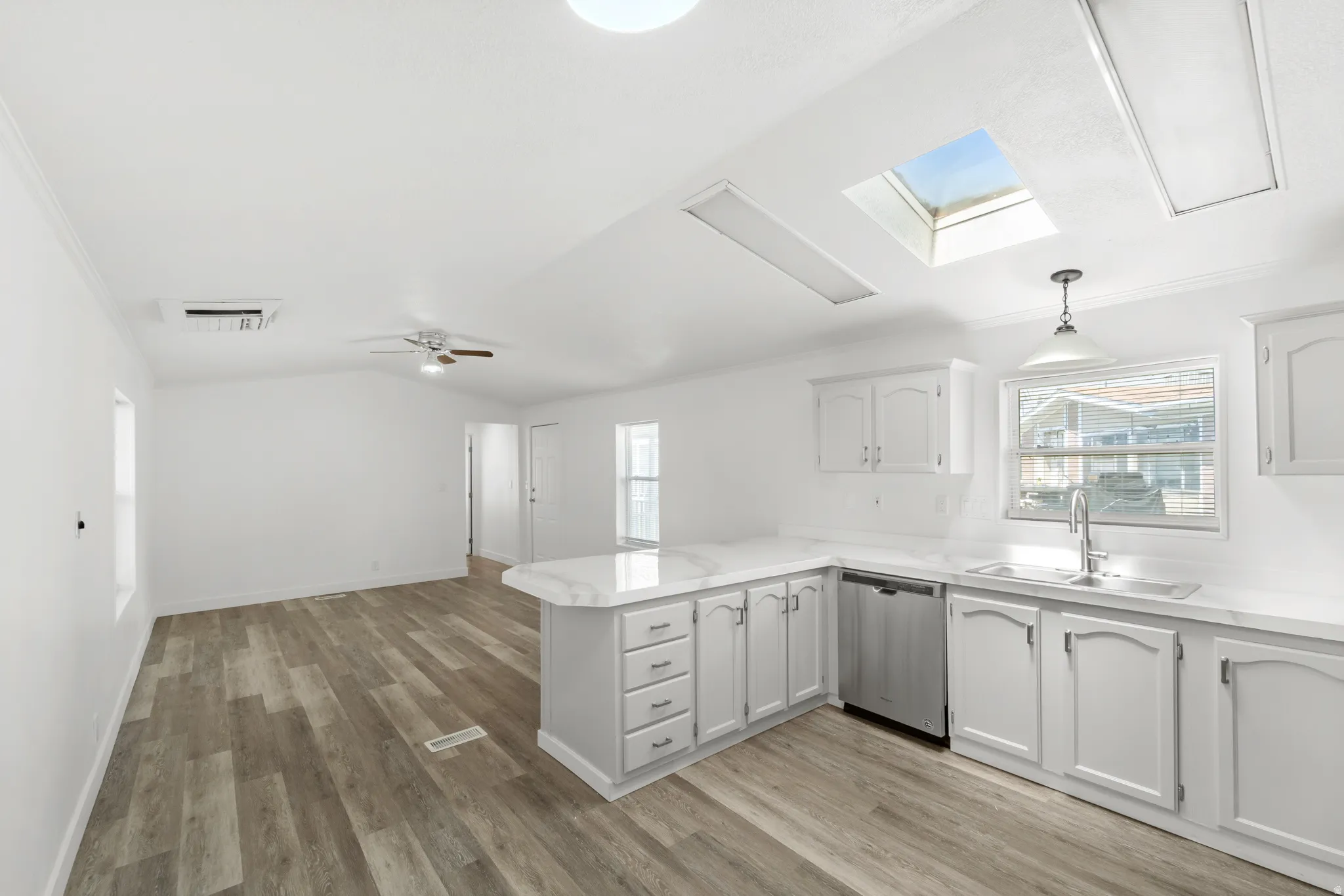 Open-concept kitchen and living area featuring wood-finish flooring, white cabinetry, a kitchen island with seating, a stainless steel dishwasher, and a skylight
