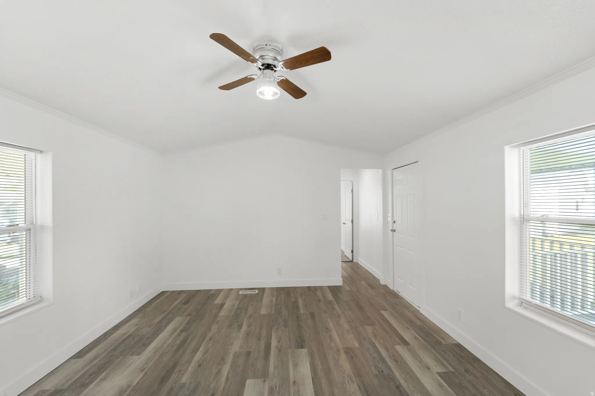Spacious room featuring wood-finish flooring, vaulted ceiling, and two windows with blinds