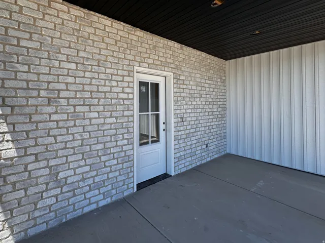 Exterior patio featuring light-toned brickwork, a white paneled door with window inserts, and a dark soffit