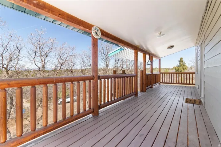 Expansive covered porch featuring wood-finish decking, natural wood railings, and a light-colored siding exterior