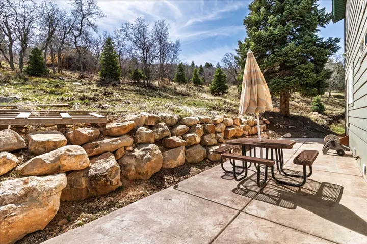 Concrete patio with a natural stone retaining wall, bordered by natural landscaping and mature trees
