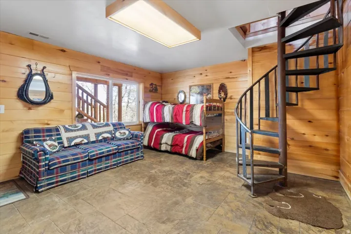 Warm wood-paneled room featuring a metal spiral staircase, tiled flooring, and a large window with natural light