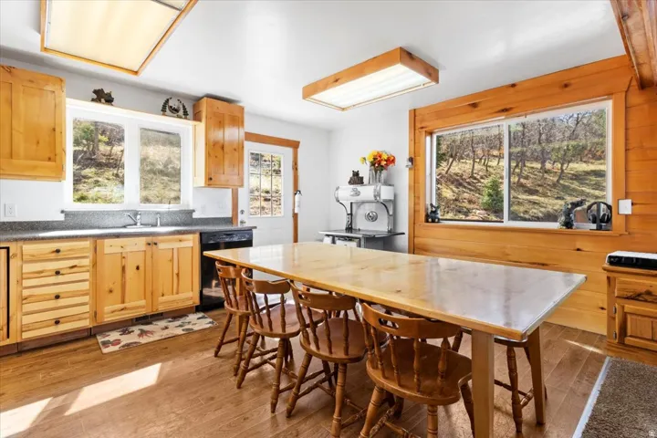Spacious kitchen featuring natural wood cabinetry, wood-finish flooring, a large island with seating, dark countertops, and a double basin sink