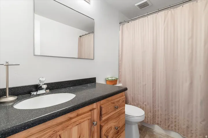 Bathroom featuring a wood-finish vanity with a dark speckled countertop, an undermount sink, and a framed mirror