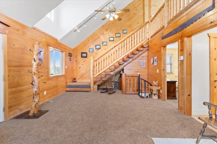 Vaulted ceiling with skylight, exposed wood paneling, wood-finish staircase, track lighting, and a ceiling fan