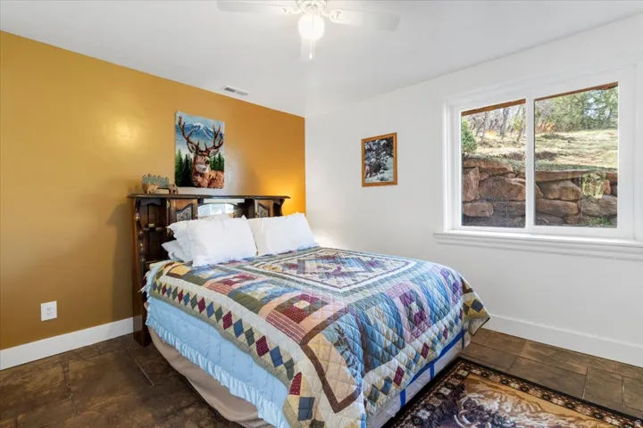 Bedroom featuring a dual-tone paint scheme, a white ceiling fan, tile flooring, and a window with a stone retaining wall outside