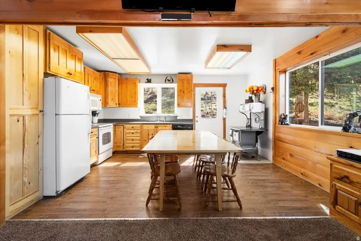 Kitchen featuring abundant natural wood cabinetry, wood-finish flooring, white appliances, and a window overlooking exterior greenery