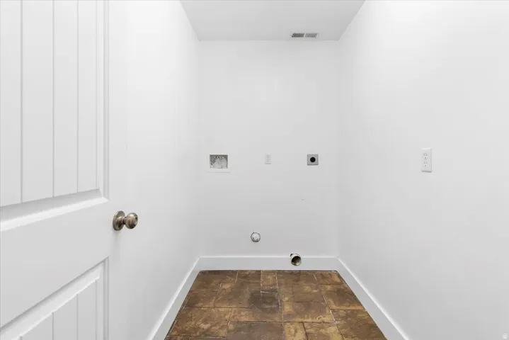 Utility space with neutral wall paint, brown-toned floor tiles, and a beadboard-style door