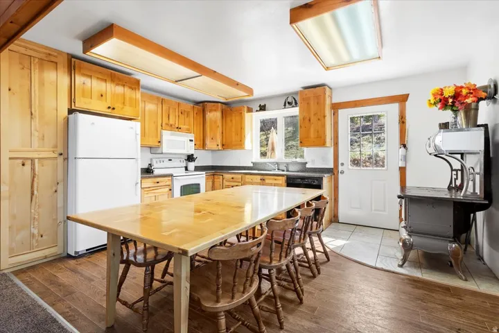 Kitchen featuring wood-finish flooring, natural wood cabinetry, and a complete suite of white appliances