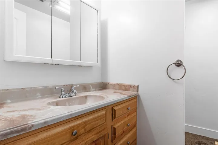 Bathroom vanity featuring a light-toned stone countertop with an integrated sink, dual-handle faucet, and natural wood-finish cabinetry