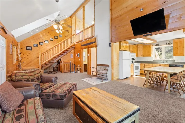 Open-concept living space featuring wood paneling, a vaulted ceiling, and a prominent staircase with wood railings