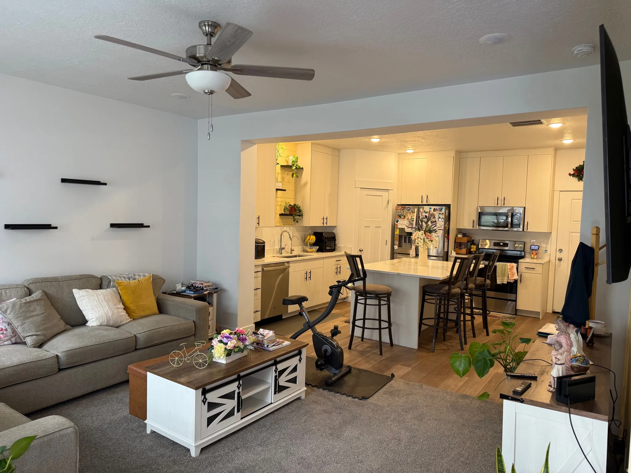 Open-concept living space featuring a ceiling fan with light fixture, carpeted living area, and wood-finish flooring