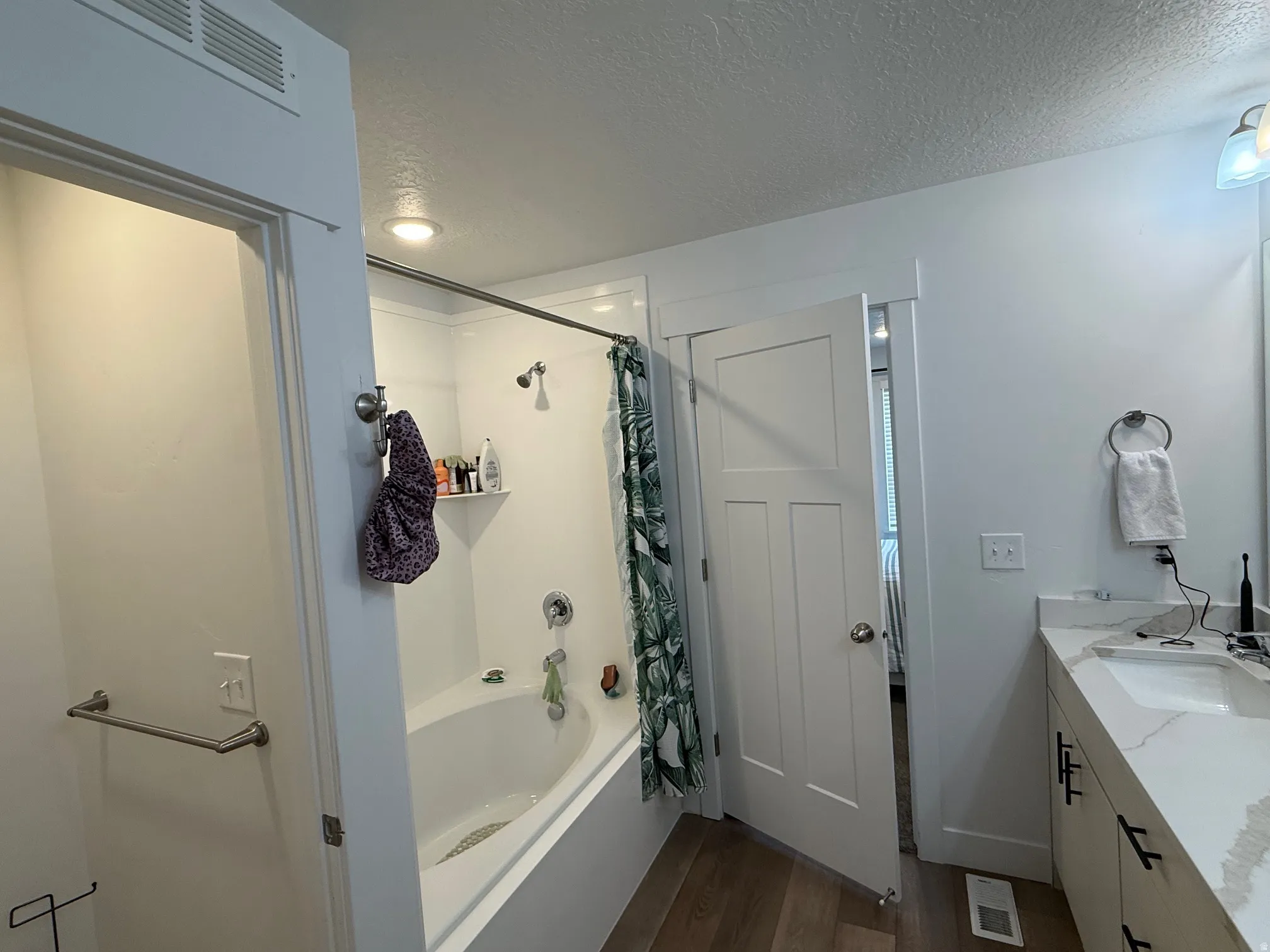 Bathroom featuring a white bathtub with an integrated shower, wood-finish flooring, a white vanity with an undermount sink, quartz countertop, and a contemporary panel door