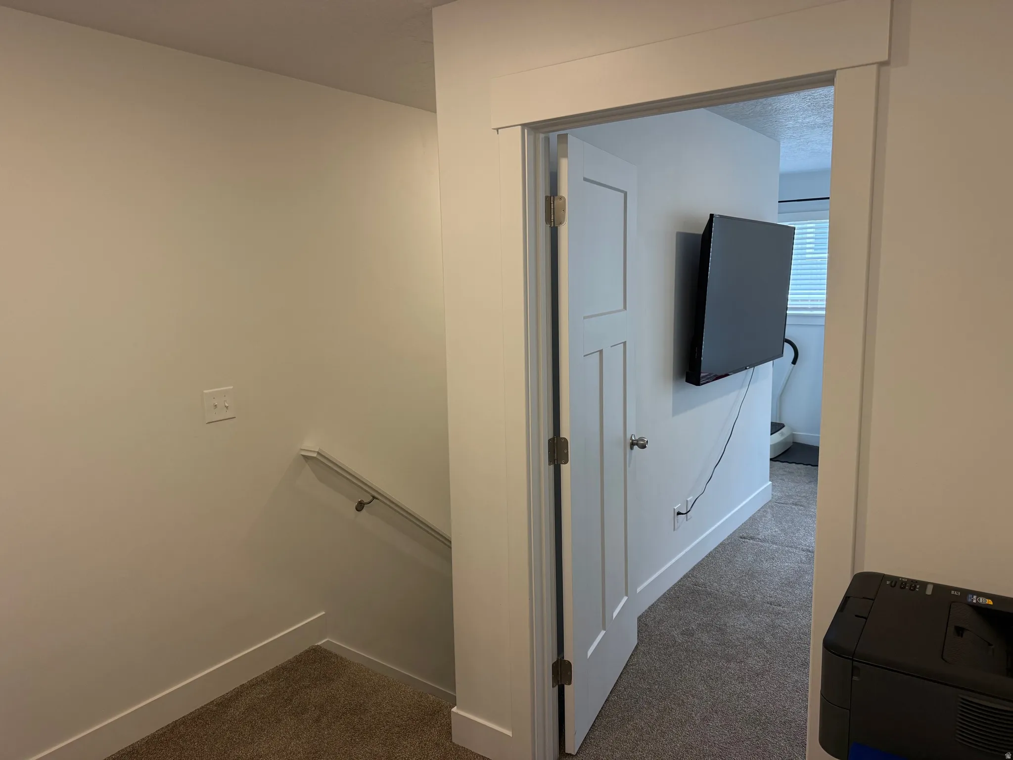 Bright white walls and trim frame a doorway leading to a carpeted room with a wall-mounted television