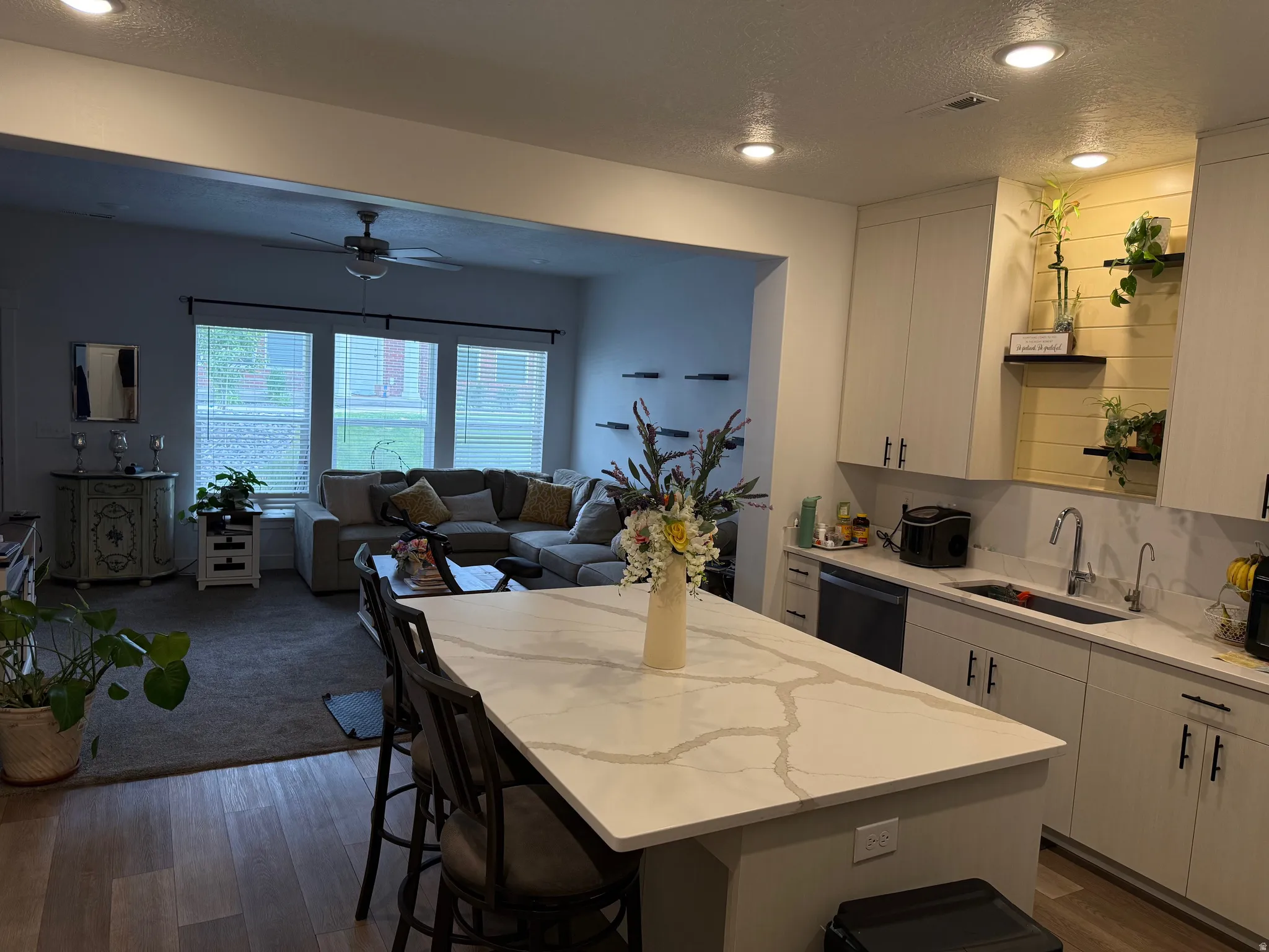 Open-concept kitchen featuring a large island with a light-toned countertop, white cabinetry with dark hardware, and a built-in sink