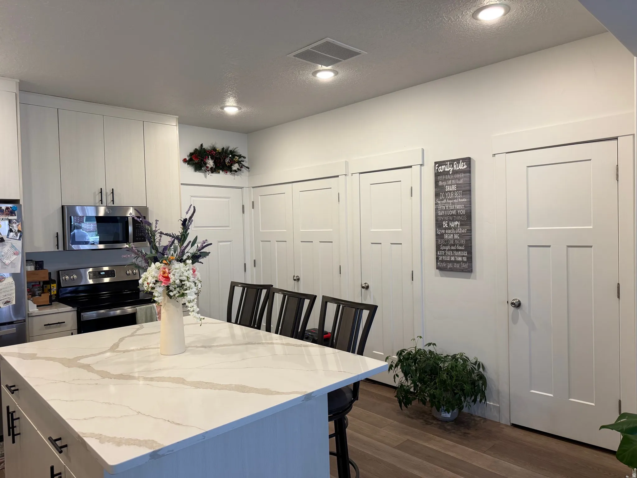 Kitchen featuring a large island with a light-toned countertop, stainless steel appliances, white flat-panel cabinetry, recessed lighting, and wood-finish flooring