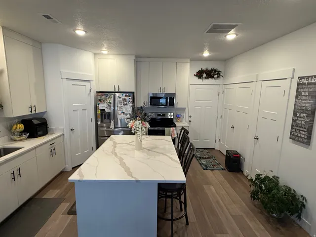 Modern kitchen featuring a large central island with a waterfall-edge countertop, light wood-finish flooring, recessed lighting, white cabinetry, and stainless steel appliances
