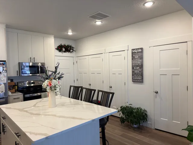 Kitchen featuring a large island with a light-toned countertop, stainless steel appliances, white flat-panel cabinetry, recessed lighting, and wood-finish flooring